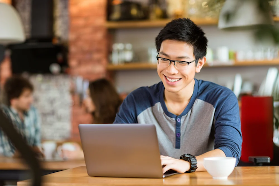 Happy cheerful young asian male in glasses smiling and using stemble in cafe copy